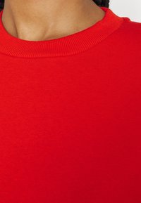 Röd bomullströja med ribbad rund hals och slät, mjuk textur. Tyget verkar lättviktigt med en enhetlig färg.