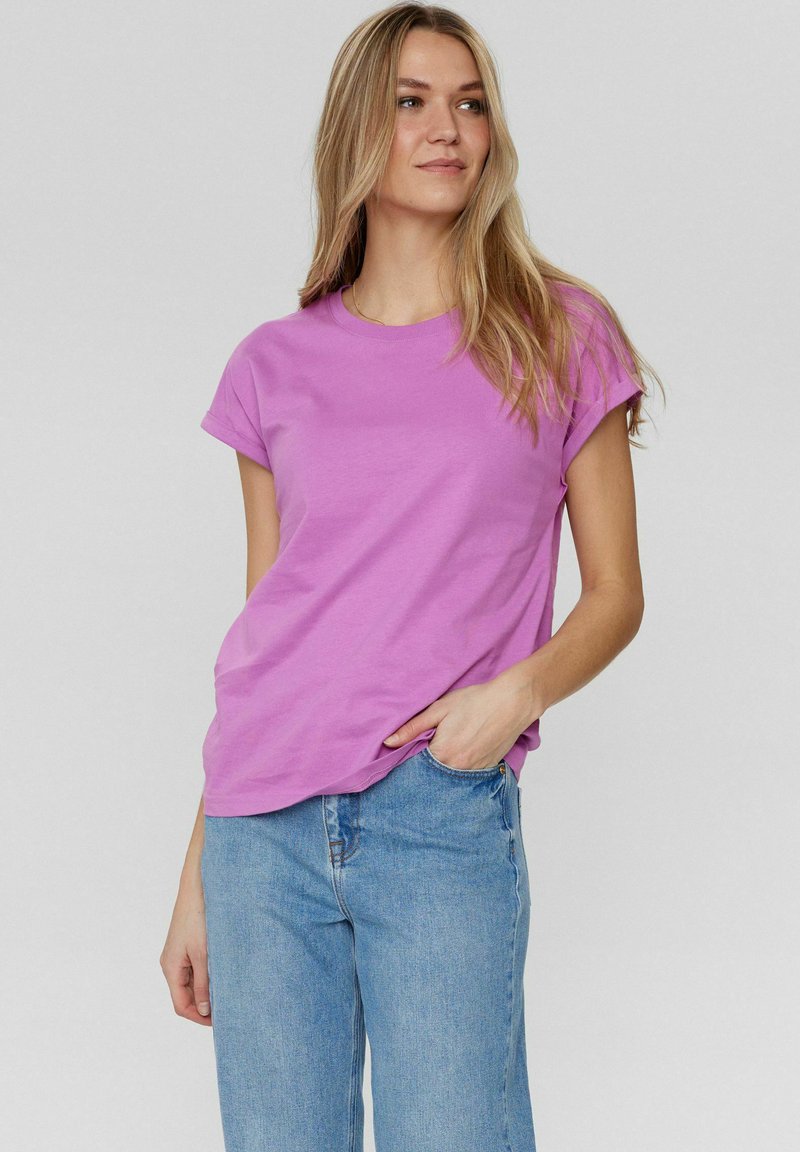 Korte mouwen, T-shirt met ronde hals in felpaars katoen. Gekoppeld met lichtblauwe jeans, met een relaxte pasvorm en lichte slijtage.