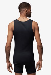 Zwarte tanktop gemaakt van een gladde, rekbare stof. Heeft een ronde hals en wordt gecombineerd met zwarte shorts. Zichtbare tatoeages op de armen.