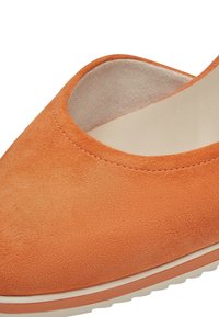 Ballerines en daim orange avec une texture lisse, un bout arrondi et une semelle en caoutchouc blanche basse. Présente un design avec des découpes sur le côté.