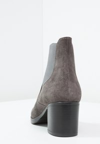 Stivaletti alla caviglia in suede grigio con pannelli laterali elasticizzati e tacco a blocco nero, visti da dietro. Texture liscia e design semplice.