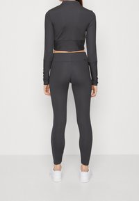 Svart kortärmad topp med långa ärmar och matchande åtsittande leggings gjorda av mjukt, elastiskt material. Accenterad med subtil branding. Vita sneakers.