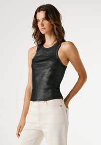 Μαύρο, εφαρμοστό τοπ χωρίς μανίκια από γυαλιστερό, υφασμάτινο ύφασμα με υφή. Έχει στρογγυλή λαιμόκοψη και φαρδιές τιράντες, συνδυασμένο με ανοιχτόχρωμο τζιν.