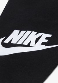 Čierna tkanina s výrazným bielym logom Nike, ktoré obsahuje dizajn švihu. Materiál má hladkú textúru, čo zabezpečuje čistý vzhľad.