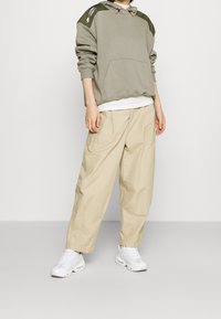 Sudadera gris con acentos verdes, bolsillo frontal y cordón. Combinada con pantalones cargo sueltos beige. Zapatillas blancas completan el conjunto.