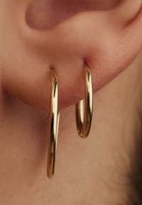 Boucles d'oreilles créoles dorées avec une finition lisse et polie, suspendues à un lobe d'oreille, présentant deux créoles circulaires de tailles différentes.
