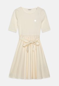 Kermanvärinen ribbineulospuseromekko, jossa on laskostettu silkin kaltainen hameosa, vyötärönauhakiinnitys ja pieni logo rinnassa.