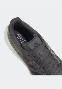 Chaussure de sport gris foncé avec lacets, col rembourré, dessus en tissu texturé et semelle blanche, vue en plongée inclinée.