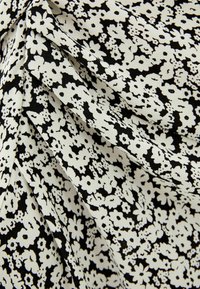 Mustavalkoinen kukkakuvioinen kangas, jossa on pieniä painettuja kukkia ja lehtiä vaihtelevilla kuvioilla, kankaan laskostus esittelee tekstuuria ja pehmeyttä.