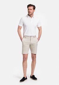Witte heren polo met drie knopen, gecombineerd met beige shorts en zwarte instappers. Eenvoudig ontwerp en ademend materiaal.