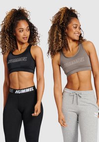 Czarne i szare sportowe biustonosze z logo "HUMMEL", charakteryzujące się gładką teksturą i designem z racerback. Wyeksponowane czarne legginsy i szare dresy.