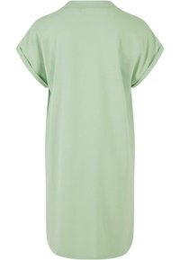 Lys grønn oversized t-skjortekjole laget av myk stoff, med korte rullede ermer og en enkel, ren silhuett.