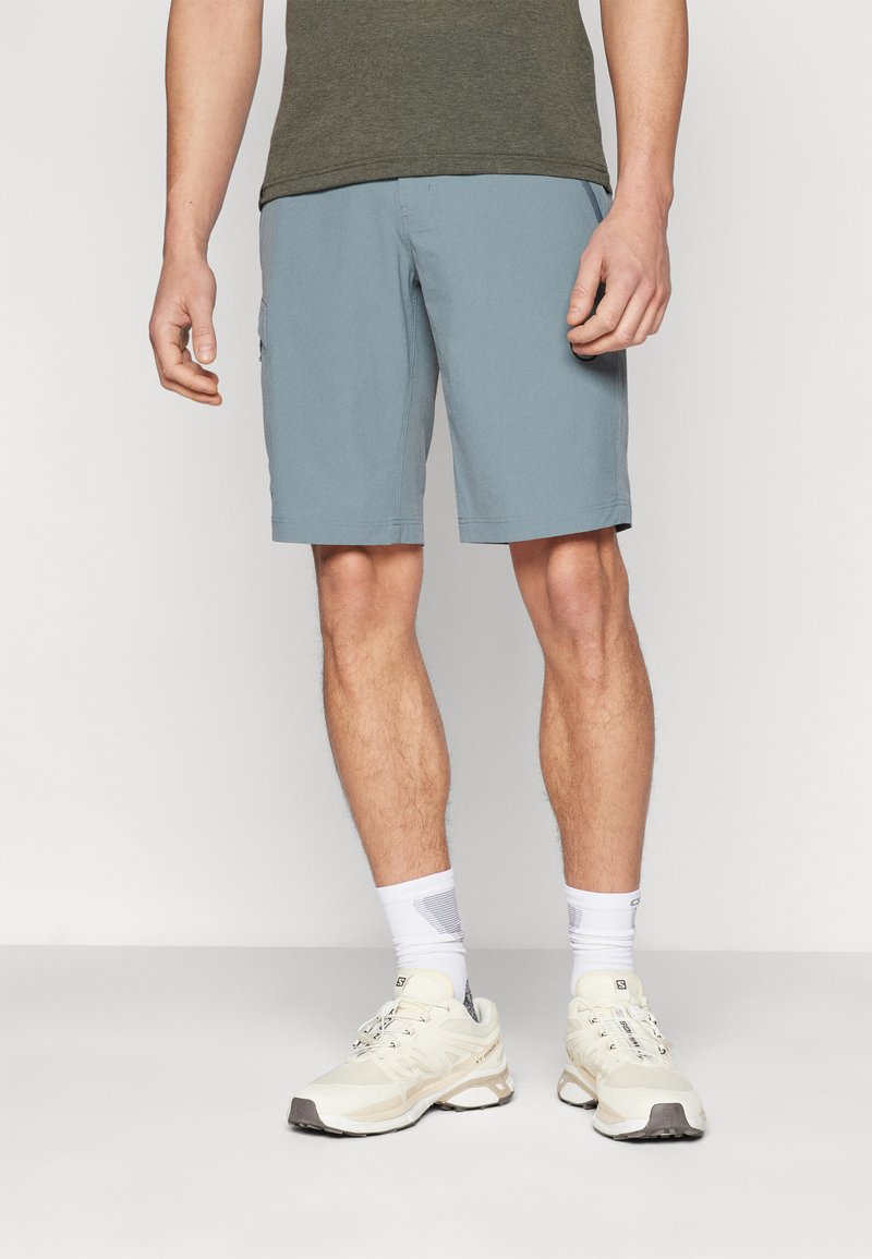 Himmelblaue Shorts mit geradem Schnitt, ausgestattet mit Seitentaschen und einer glatten Textur, kombiniert mit cremefarbenen Sneakers und weißen Socken.