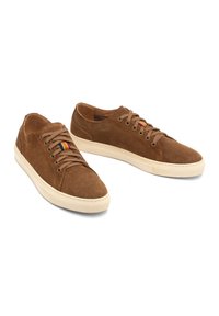 Baskets en suède marron avec semelle en caoutchouc beige, bout rond, fermeture lacée et une petite bande multicolore sur le côté.