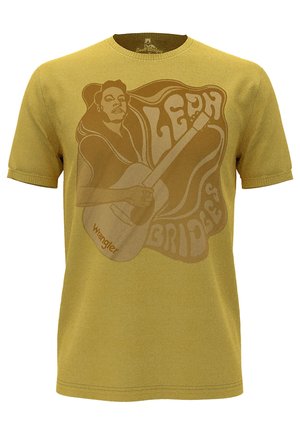 T-shirt jaune à manches courtes avec un imprimé graphique d'une femme jouant de la guitare, avec le texte "Leah Bridges" et le logo "Wrangler" en marron.