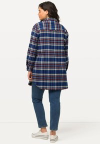 Blauwe geruite blouse met lange mouwen, voorzien van witte, rode en groene ruitpatronen. Gemaakt van een zachte stof, heeft het een gebogen zoom en een label aan de achterkant.