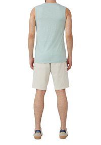 Helles blaues ärmelloses Shirt, weiche Textur, kombiniert mit cremfarbenen Shorts, lässige Passform, Modell mit dem Rücken zur Kamera, trägt beigen Schuhe mit blauen Akzenten.