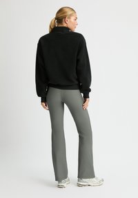 Pullover in pile nero con colletto alto, abbinato a pantaloni slim-fit verde oliva. L'outfit presenta polsini a coste e tessuto testurizzato.