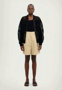 Must mustrakk särk, millel on must pits ja soonikuga varrukad, kombineeritud sobiva musta toppi ja beežide lühikeste pükstega. Mudel seisab neutraalses taustas.