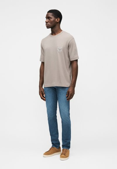 Gray cotton t-shirt with a chest pocket, paired with blue denim jeans. The outfit is completed with tan suede sneakers.
