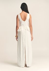 Robe en lin blanc avec une taille peplum, un dos en V profond et une fente sur le côté. Design minimaliste avec une texture subtile et des lignes épurées.