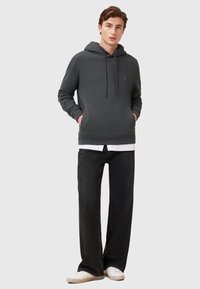 Grauer Baumwoll-Hoodie mit Kängurutasche und Kapuze mit Kordelzug, kombiniert mit schwarzen weiten Jeans und weißen Sneakern.