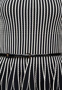 Μαύρο και λευκό κάθετο ριγέ εφαρμοστό φόρεμα με λεπτή μαύρη ζώνη στη μέση, με υφασμένα ανάγλυφα σχέδια σε ρίγες.