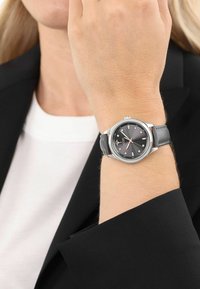 Silberne Uhr mit einem dunkelgrauen Ziffernblatt und Edelstahlgehäuse, ausgestattet mit einem strukturierten grauen Lederarmband und rhombusformigen Stundenmarkierungen.