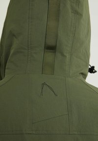Veste à capuche vert olive vue de dos avec bande verticale cousue et petite broderie abstraite en ligne sous la capuche.
