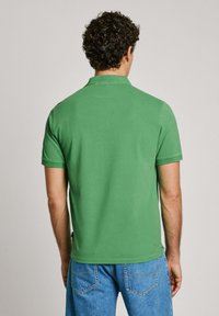 Green polo shirt with short sleeves, finished with a classic collar. Cotton fabric, smooth texture, and a fitted design. Worn with blue jeans.