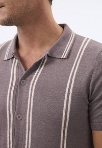 Polo gris avec des rayures blanches verticales, un col classique et une patte de boutonnage à deux boutons. Texture douce et manches courtes.