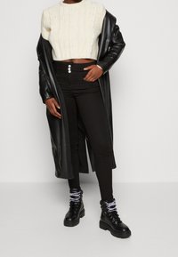 Krämfärgad kabelstickad cropped tröja, svarta högmidjade skinny jeans med treknappsstängning, och svarta snörade ankelskor med lila snören.