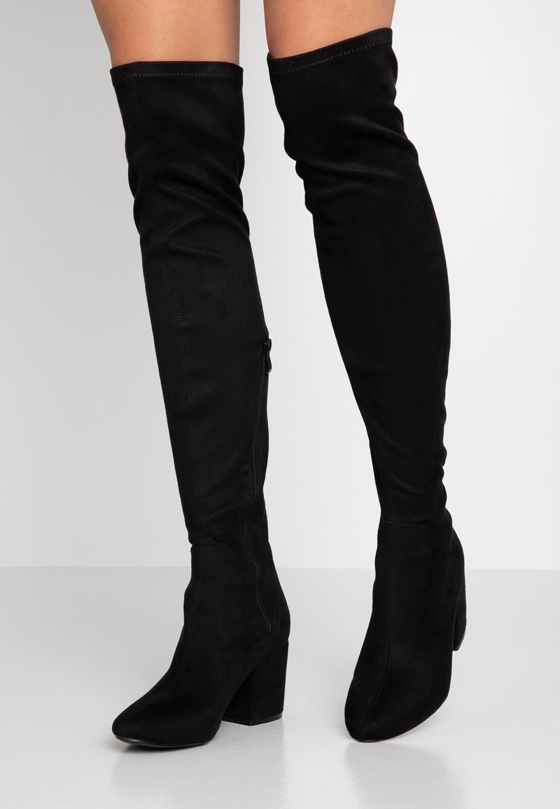 Bottes noires en daim au-dessus du genou avec un bout pointu et un talon bloc. Dotées d'une fermeture éclair latérale et d'une texture lisse.