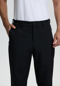 Pantalones negros hechos de una tela suave y elástica, con una parte delantera plana, cremallera y bolsillos laterales. Cuenta con un ajuste entallado y presillas para cinturón.