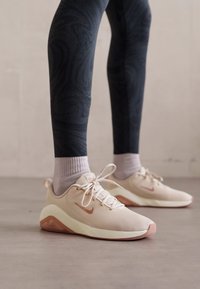 Lichtbeige sport schoenen met een bovenwerk van mesh, oranje accenten en een getextureerde zool. Gecombineerd met donkere met patronen bedrukte leggings en lichte sokken.