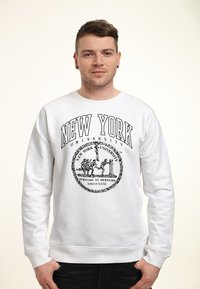 Weißer Pullover mit schwarzem Grafikdruck "NEW YORK UNIVERSITY" und Emblem mit Figuren und Text. Weicher Stoff, Rundhalsdesign.