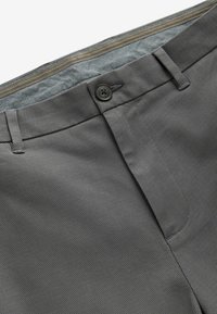 Pantalones grises texturizados con cierre de botón, que presentan un forro a cuadros en la cintura y un acabado suave en la tela exterior.