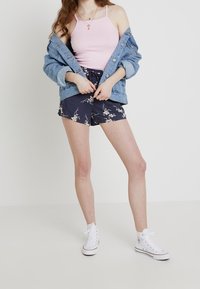 Light pink tank top, denim jacket, and navy floral shorts; white high-top sneakers complete the outfit with casual, textured style.