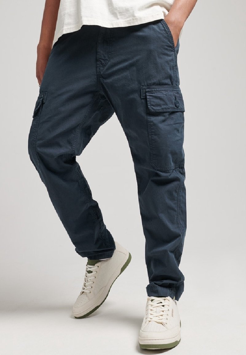 Pantalones cargo de tela azul oscuro, con bolsillos laterales y un corte holgado. Combinados con zapatillas crema con acentos verdes.