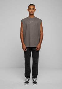 Grå ärmlös t-shirt med rund halsringning och kursiv logotyp, i kombination med svarta byxor och svarta sneakers. Enkelt och avslappnat design.