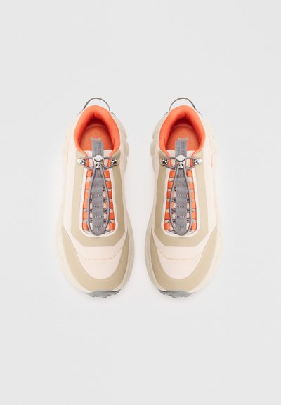 Beige and cream sneakers with an orange inner lining, featuring a grey elastic lacing system and textured sole. Rounded, padded design.