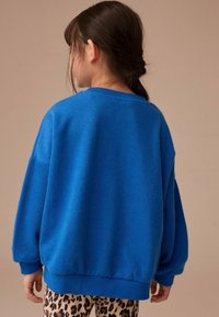 Blauer Fleece-Pullover mit lockerer Passform, featuring über die Schultern geschnittenen Ärmeln und gerippten Bündchen. Kombiniert mit einer Hose im Leopardenmuster.