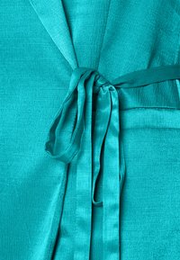 Robe turquoise avec une finition texturée, dotée d'une ceinture nouée à la taille et d'un tissu lisse et fluide. Les accents comprennent un léger éclat et un drapé élégant.