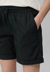 Pantalones cortos negros de tiro alto fabricados con tejido ligero, con cintura elástica, bolsillos laterales y dobladillos enrollados. Textura suave.