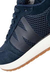 Marinblå atletik sneakers med ovandel i mesh och mockadetaljer, ett distinkt logotyp, platta snören och en vit mellansula med en sula i gummi.