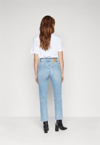 Ljusblå denimjeans med rak passform, prydda med en brun etikett vid midjan, fransig nederkant, ihop med en vit t-shirt och svarta stövlar.