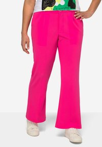 Pantalons évasés roses en tissu lisse avec poches avant, associés à des baskets blanches. Le design présente un devant plat avec des plis.