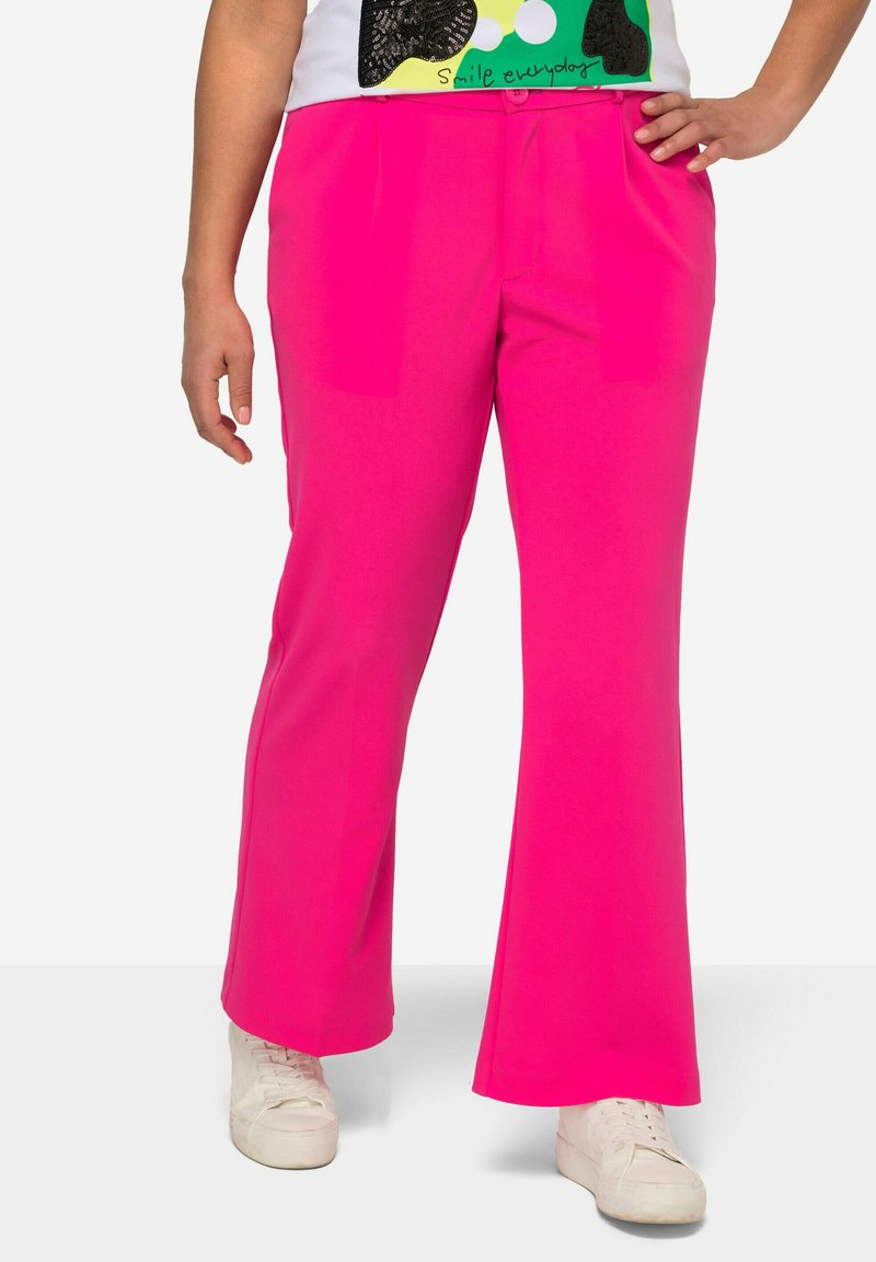 Rosa utsvängda byxor i ett smidigt tyg med framfickor, kombinerat med vita sneakers. Designen har en platt front med veck.