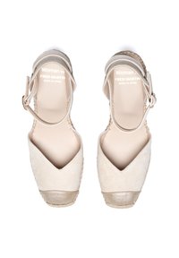 Espadrilles compensées en suède beige avec un bout pointu, un embout doré métallique et une lanière au niveau de la cheville avec une boucle métallique. Fabriquées en Espagne.