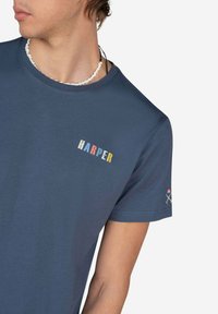 Camiseta de algodón azul marino con mangas cortas, que presenta el texto multicolor "HARPER" en el pecho y un pequeño gráfico en la manga.